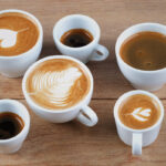 Different espresso drinks showing the difference between latte cappuccino and macchiato served in white cups on a wooden table