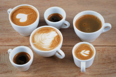 Different espresso drinks showing the difference between latte cappuccino and macchiato served in white cups on a wooden table