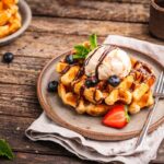 Belgian waffles vs pancakes featuring an Icki Sticki Belgian waffle topped with banana whipped cream and pecans