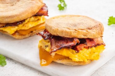 Breakfast sandwich filling with scrambled egg bacon and melted cheddar cheese on a toasted English muffin