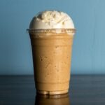 What is a frappe showing a thick blended coffee drink topped with whipped cream in a large cafe cup