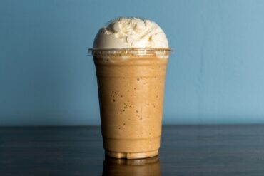 What is a frappe showing a thick blended coffee drink topped with whipped cream in a large cafe cup