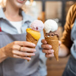 Two staff members holding waffle cones with multiple scoops at the best ice cream shop in Wisconsin