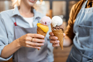 Two staff members holding waffle cones with multiple scoops at the best ice cream shop in Wisconsin