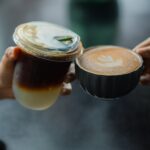 Two hands holding a hot latte vs iced latte at a café counter