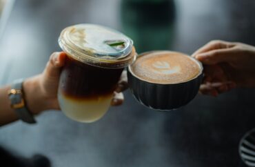 Two hands holding a hot latte vs iced latte at a café counter
