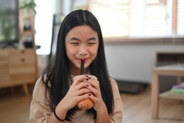 What is boba tea showing a young girl enjoying a boba tea drink with tapioca pearls and wide straw