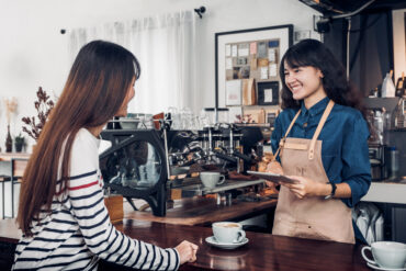 Barista and customer smiling at the counter, an example of good coffee shop etiquette during an order
