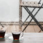 Two steaming cups of coffee on a table with rain streaking down the window, a rainy day coffee order in Verona, WI