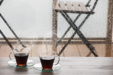 Two steaming cups of coffee on a table with rain streaking down the window, a rainy day coffee order in Verona, WI